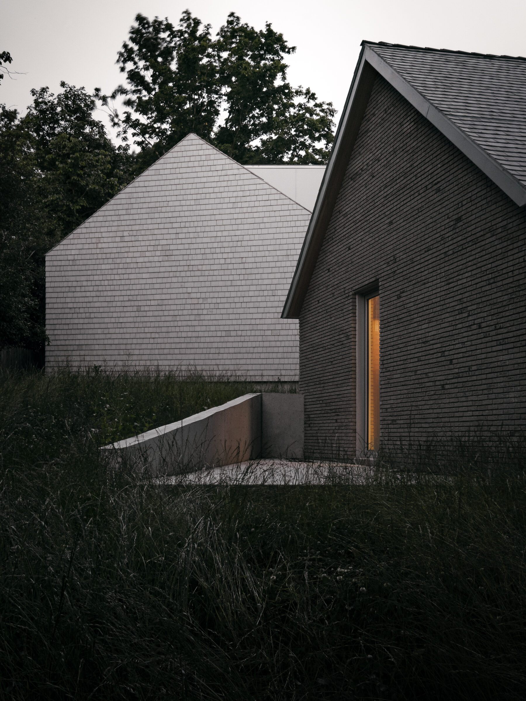 Twin gables at dusk, a single window glowing from within