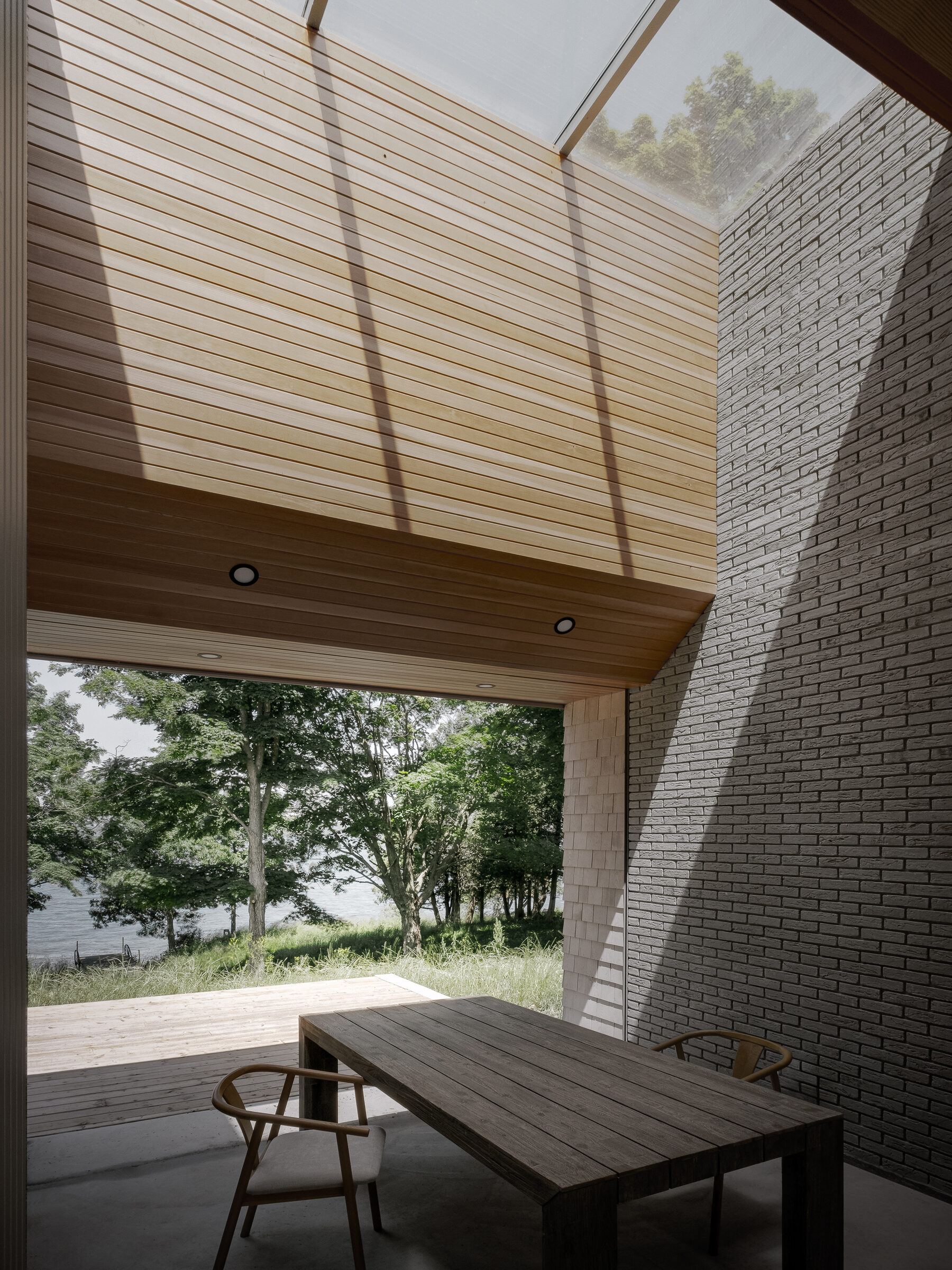 Dining table under a cedar-lined overhang, framed by trees and the lake beyond